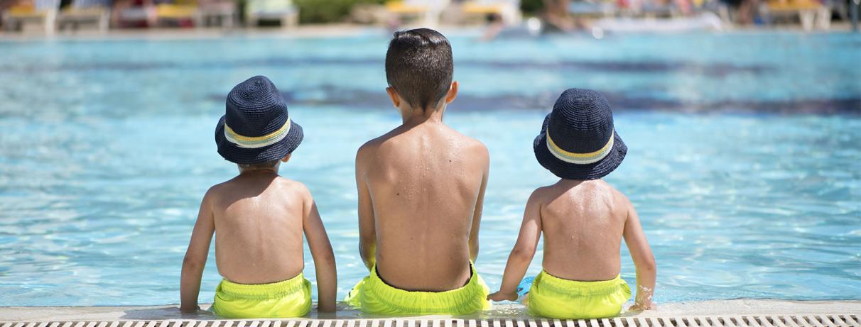 3 enfants de dos assis au bord de la piscine
